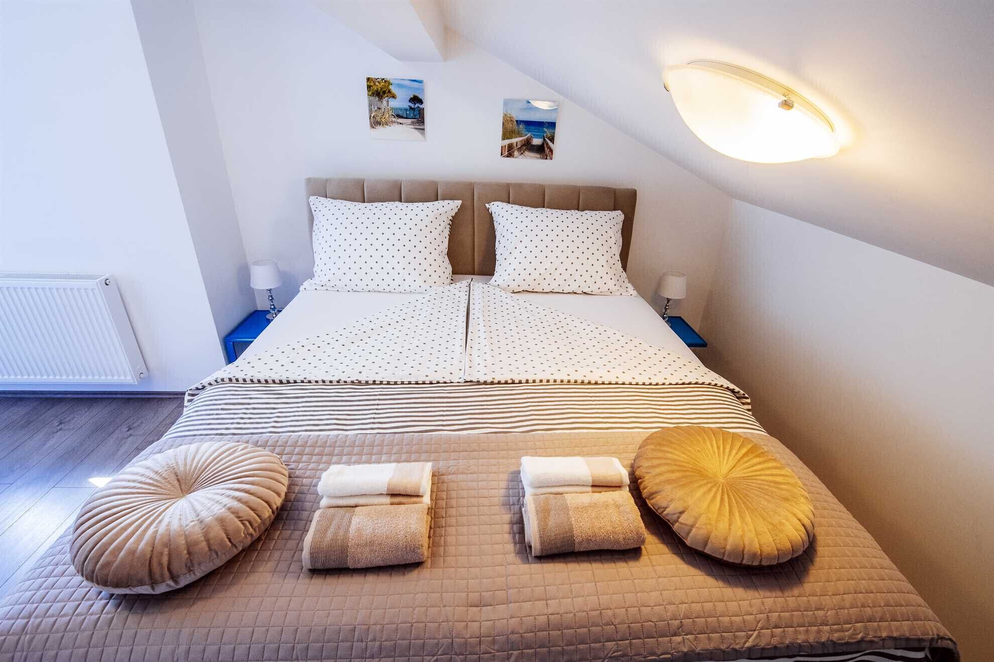 Et soveværelse med seng, to puder, et natbord, en lampe, et billed på væggen, en loftlampe og en radiator.
