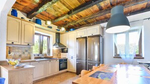 Una cocina con vigas de madera, armarios blancos, electrodomésticos de acero inoxidable y una gran mesa de comedor.
