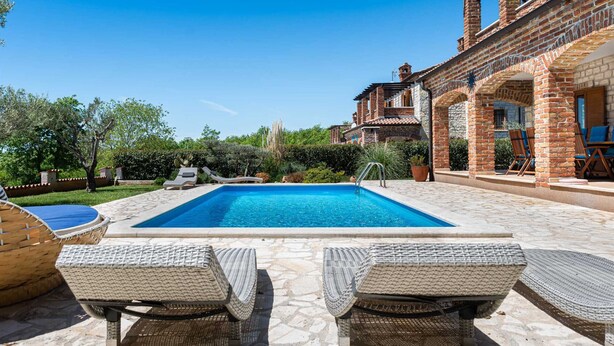 Una piscina con sillas de descanso, rodeada por un edificio de ladrillo con ventanas de arco y mobiliario exterior.