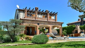 Una casa de dos pisos con fachada de ladrillo, un patio con piscina y una zona de barbacoa.