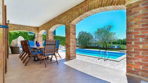 Un patio cubierto con piscina, arcos de ladrillo y mobiliario exterior.