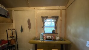 A small kitchen with a window, wooden stools, a shelf with jars, and a trash bin. - Rustic Cabin (Bayfield)