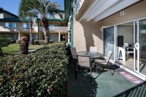 A hotel balcony with a table and chairs, a palm tree, and a view of the hotel building.