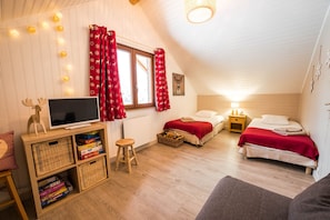 A cozy room with two beds, a TV, and a bookshelf with board games. - "Le Bois des Neiges" Charming authentic chalet  (Xonrupt-Longemer)