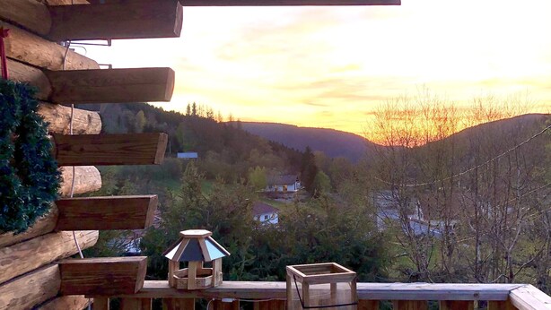 A wooden deck with a table set for two, overlooking a hilly landscape during sunset. - "Le Bois des Neiges" Charming authentic chalet  (Xonrupt-Longemer)