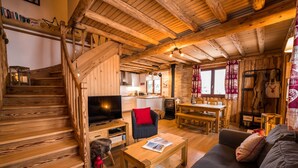 A cozy wooden cabin interior with a staircase, a living area with a sofa, a dining table, and a kitchen area. - "Le Bois des Neiges" Charming authentic chalet  (Xonrupt-Longemer)