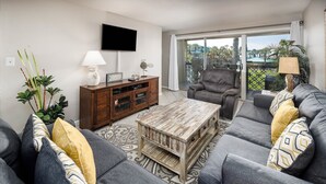 A modern living room with grey sofas, a wooden coffee table, a leather armchair, and a TV mounted on the wall. - Seaspray Condos - 100C (Fort Walton Beach)