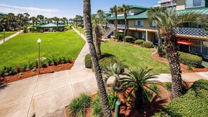 A hotel courtyard with palm trees, a well-maintained lawn, and a clear sky. - Seaspray Condos - 100C (Fort Walton Beach)