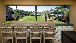 A patio with four Adirondack chairs and a table, overlooking a pool and resort buildings. - Seaspray Condos - 100C (Fort Walton Beach)