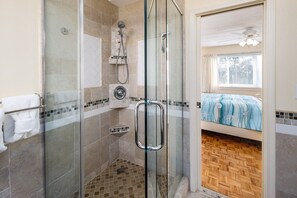 A glass-enclosed shower with a handheld showerhead and a wall-mounted faucet.