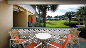 A patio area with a white table and chairs, a white lattice partition, and a view of a golf course.
