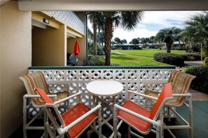 A patio area with a white table and chairs, a white lattice partition, and a view of a golf course.