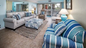 A living room with a sofa, ottoman, and armchair, a mirror, and a view through a glass door. - Seaspray Condos - 101A (Fort Walton Beach)