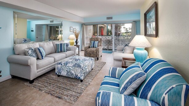 A living room with a sofa set, a patterned ottoman, a striped armchair, and a lamp.