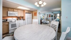 A kitchen with white cabinets, a microwave, stove, and refrigerator. There is a dining table with white chairs. - Seaspray Condos - 101A (Fort Walton Beach)