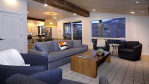 Ein modernes Wohnzimmer mit einer Couch, Sesseln, einem Couchtisch und einem großen Fenster mit Ausblick.