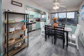 Une cuisine avec des meubles de couleur turquoise, une table à manger avec des chaises, un ventilateur de plafond et une fenêtre avec des stores.