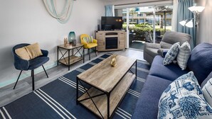 A modern living room with a sofa, armchair, coffee table, and a TV. - Seaspray Condos - 104A (Fort Walton Beach)