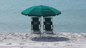 Two beach chairs under a green umbrella on a sandy beach with a calm sea in the background. - Seaspray Condos - 104A (Fort Walton Beach)