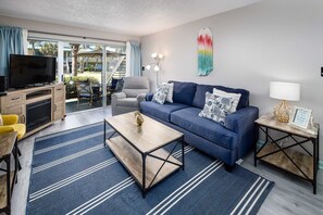 Ein modernes Wohnzimmer mit einer Couch, einem Couchtisch und einem Fernseher. Eine Glasschiebetür führt auf einen Balkon.