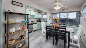 A kitchen with teal cabinets, a dining area with a white table and black chairs, and a ceiling fan. - Seaspray Condos - 104A (Fort Walton Beach)