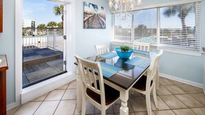 Un coin repas avec une table dressée pour quatre personnes, un bol bleu servant de centre de table et un tableau représentant une plage accroché au mur.