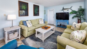 A living room with a sofa, coffee table, TV, and decorative plants. - Seaspray Condos - 102C (Fort Walton Beach)
