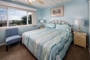 Ein Schlafzimmer mit einem großen Bett, einem Sessel, einem Nachttisch, einer Lampe und einem Fenster mit Blick.