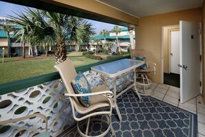 Ein Balkon mit Korbmöbeln, einem gemusterten Teppich und Blick auf ein Resort mit Palmen und Gebäuden.