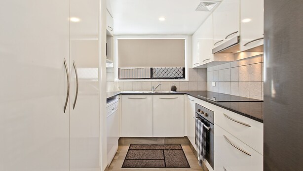 A modern kitchen with white cabinetry, a black countertop, and a built-in oven.
