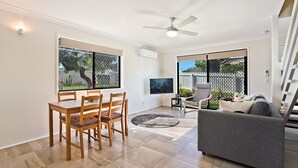 A modern living room with a dining area, a grey sofa, a ceiling fan, and a TV mounted on the wall.