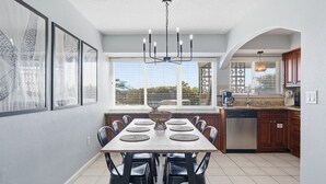 Une cuisine moderne avec un coin repas, comprenant une grande fenêtre, un lustre et un lave-vaisselle.