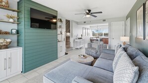 Un salon moderne avec un mur d’accent vert, un canapé gris, un ventilateur de plafond et une vue sur la salle à manger.