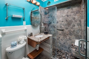 A bathroom with a stone shower wall, a white toilet, and a sink with a marble countertop.