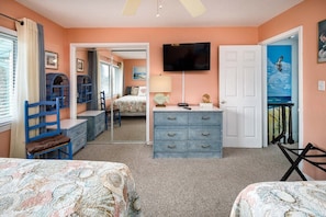 A bedroom with two beds, a dresser, a television, and a door leading to another room.