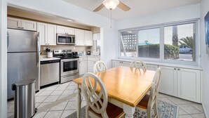 Una cocina moderna con armarios blancos, electrodomésticos de acero inoxidable y un comedor con mesa y sillas de madera.