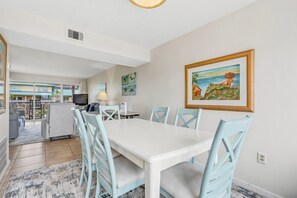 A dining area with a white table and light blue chairs, a television, and a painting on the wall.