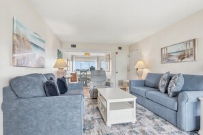 A living room with two grey sofas, a white coffee table, and a view of the outdoors.