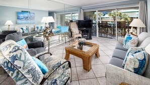 A spacious living room with a large TV, comfortable seating, and a balcony with outdoor furniture. - Seaspray Condos - 106D  (Fort Walton Beach)