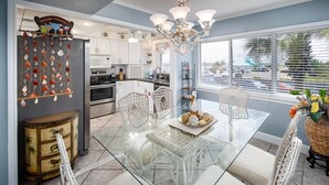 A modern kitchen with white cabinets, a glass dining table, and a decorative shell wall hanging. - Seaspray Condos - 106D  (Fort Walton Beach)