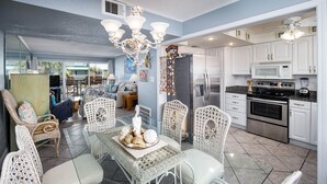 A spacious kitchen with white cabinets, stainless steel appliances, and a dining area with wicker chairs and a glass table. - Seaspray Condos - 106D  (Fort Walton Beach)