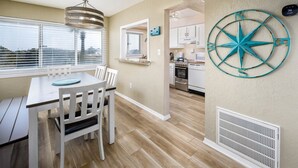 Une cuisine moderne avec des meubles blancs, un îlot central et une grande fenêtre équipée de stores.