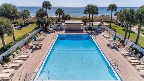 A rectangular swimming pool with a deck, surrounded by lounge chairs and palm trees, with a view of the ocean.