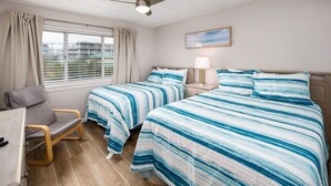 A hotel room with two beds, a desk, a chair, a ceiling fan, and a window with curtains.