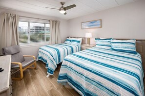 Une chambre d’hôtel avec deux lits, un bureau, une chaise, un ventilateur de plafond et une fenêtre avec des rideaux.