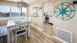 A dining area with a table and chairs, a kitchen in the background, and a wall-mounted compass decoration.