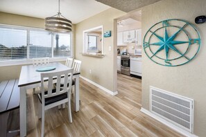 Un coin repas avec une table et des chaises, une cuisine en arrière-plan et une décoration murale en forme de boussole.