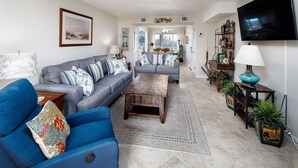 Ein Wohnzimmer mit zwei Sofas, einem Couchtisch und einem Fernseher. Im Hintergrund ist ein Essbereich zu sehen.