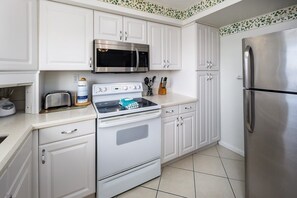 Eine Küche mit weißen Schränken, einem Edelstahl-Kühlschrank, einer Mikrowelle, einem Herd und einem Toaster.