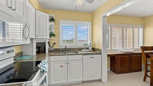 A kitchen with white cabinets, a granite countertop, a built-in oven, a dishwasher, and a ceiling fan. - Seaspray Condos - 110D (Fort Walton Beach)